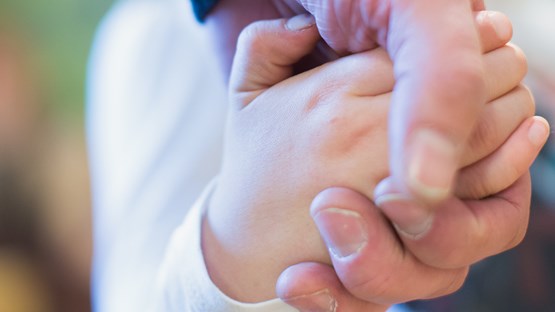 Närbild på barnhand som håller i vuxenhand.